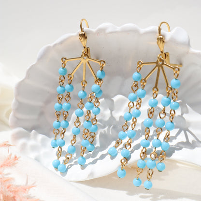 Gold and blue beaded earrings on a white shell background