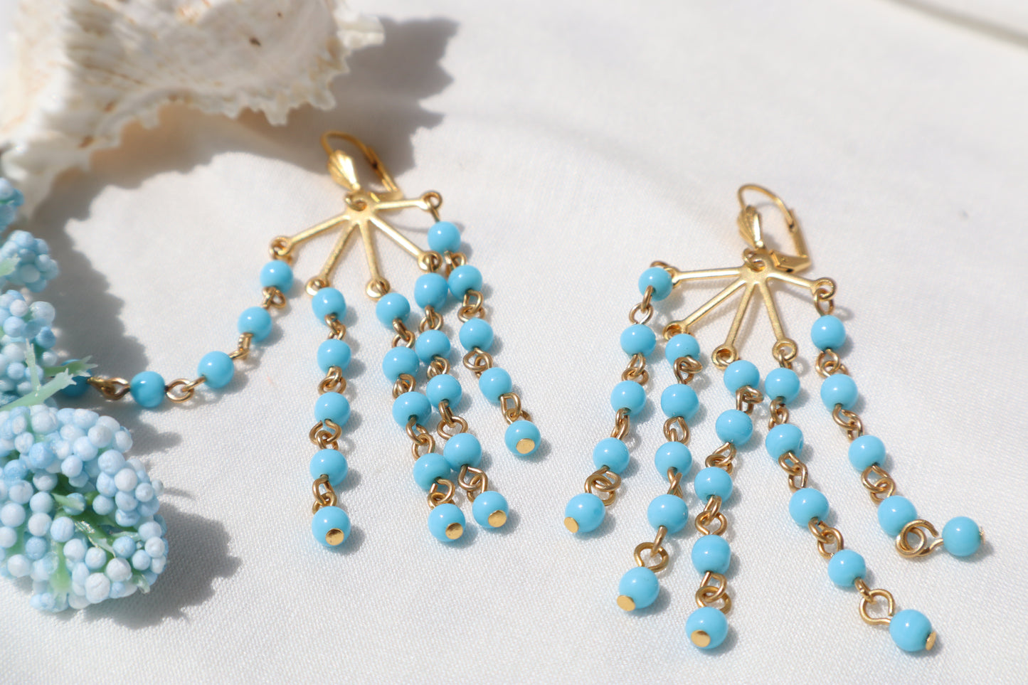 Pair of blue beaded earrings with gold accents on a white surface.