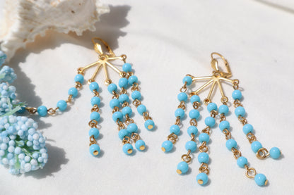 Pair of blue beaded earrings with gold accents on a white surface.