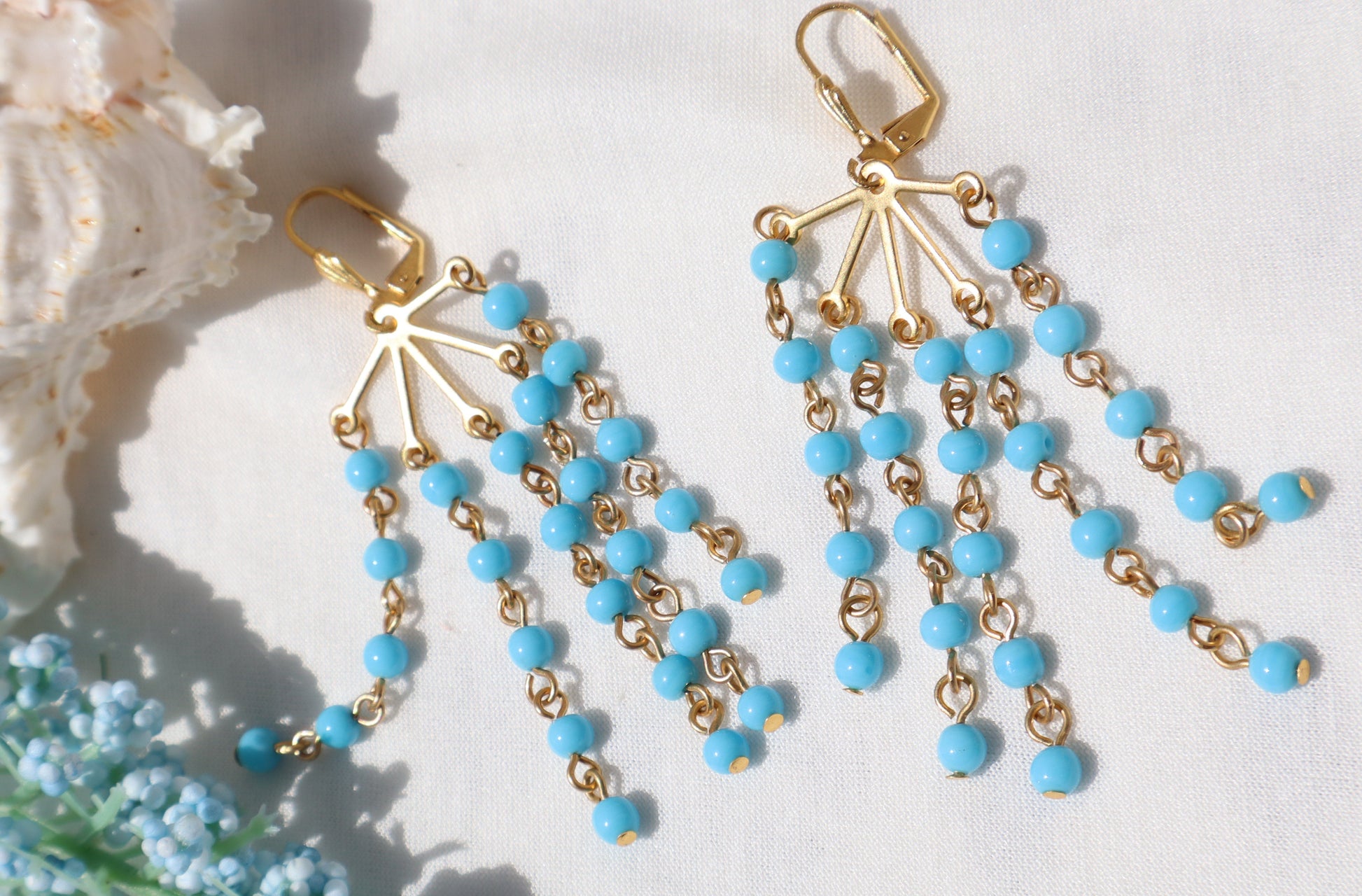 Gold and turquoise beaded earrings on a white background with floral elements.