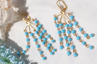Gold and turquoise beaded earrings on a white background with floral elements.