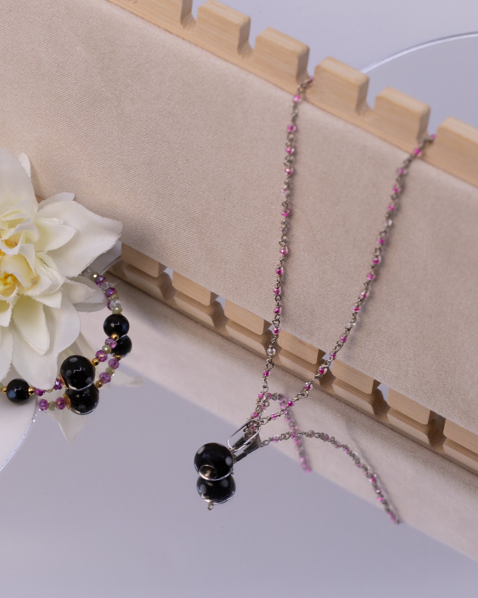 Necklace with black and pink beads on a wooden stand with a white flower.