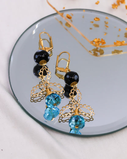 Pair of earrings with gold, black, and blue beads on a reflective surface.