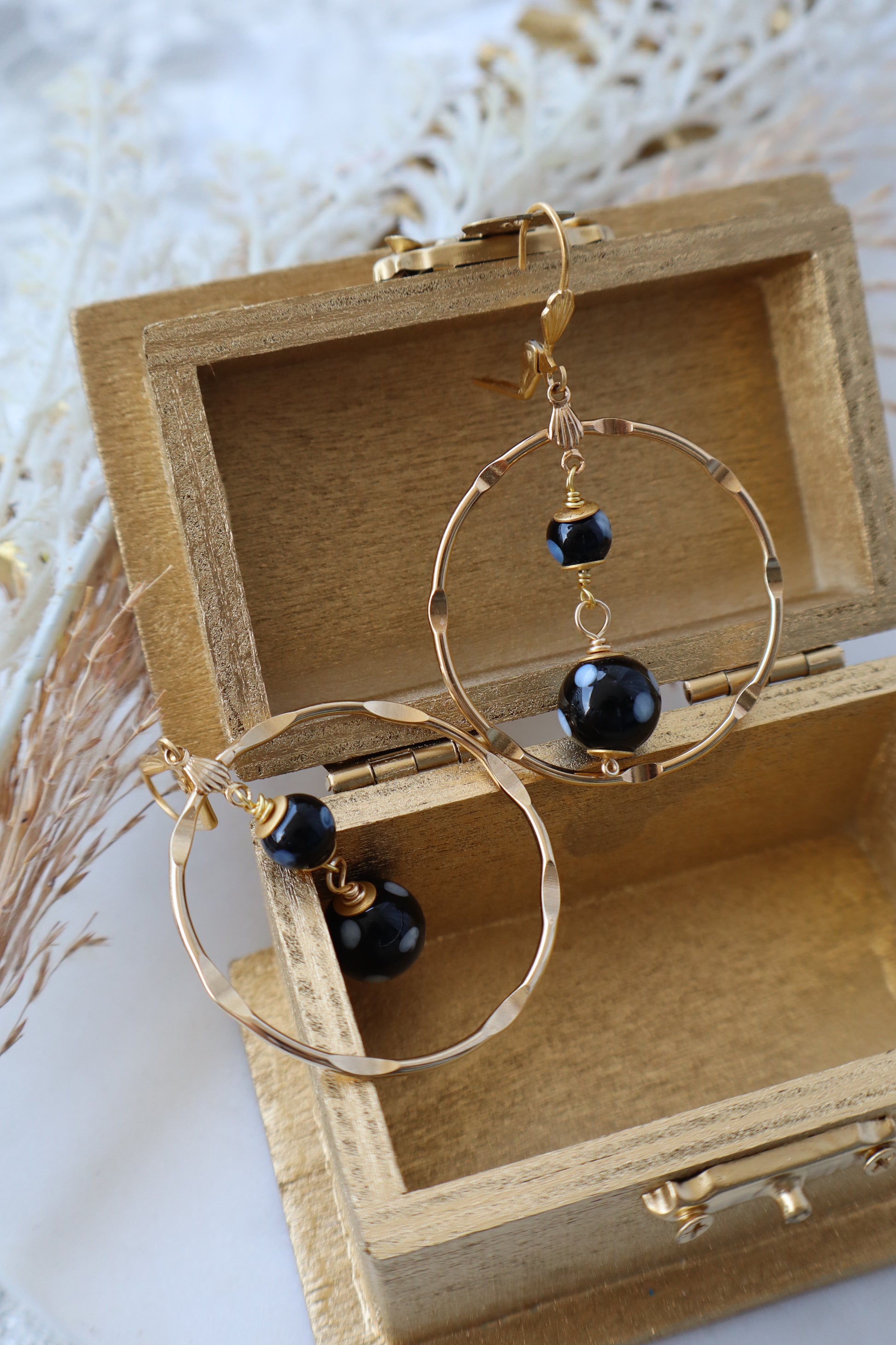 Gold hoop earrings with black beads in a wooden box on a light background