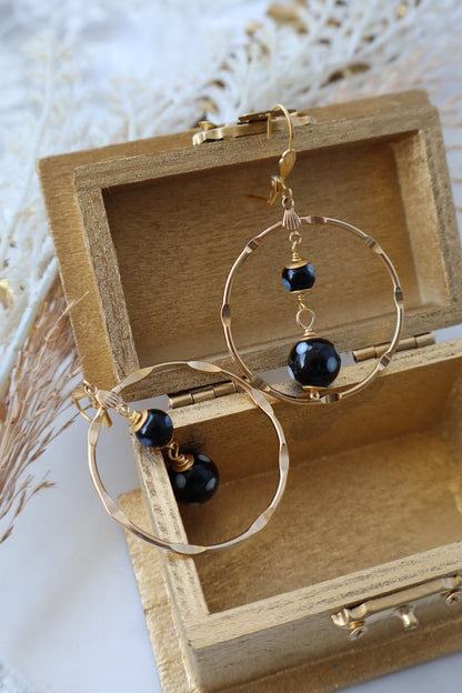 Gold hoop earrings with black beads in a wooden box on a light background