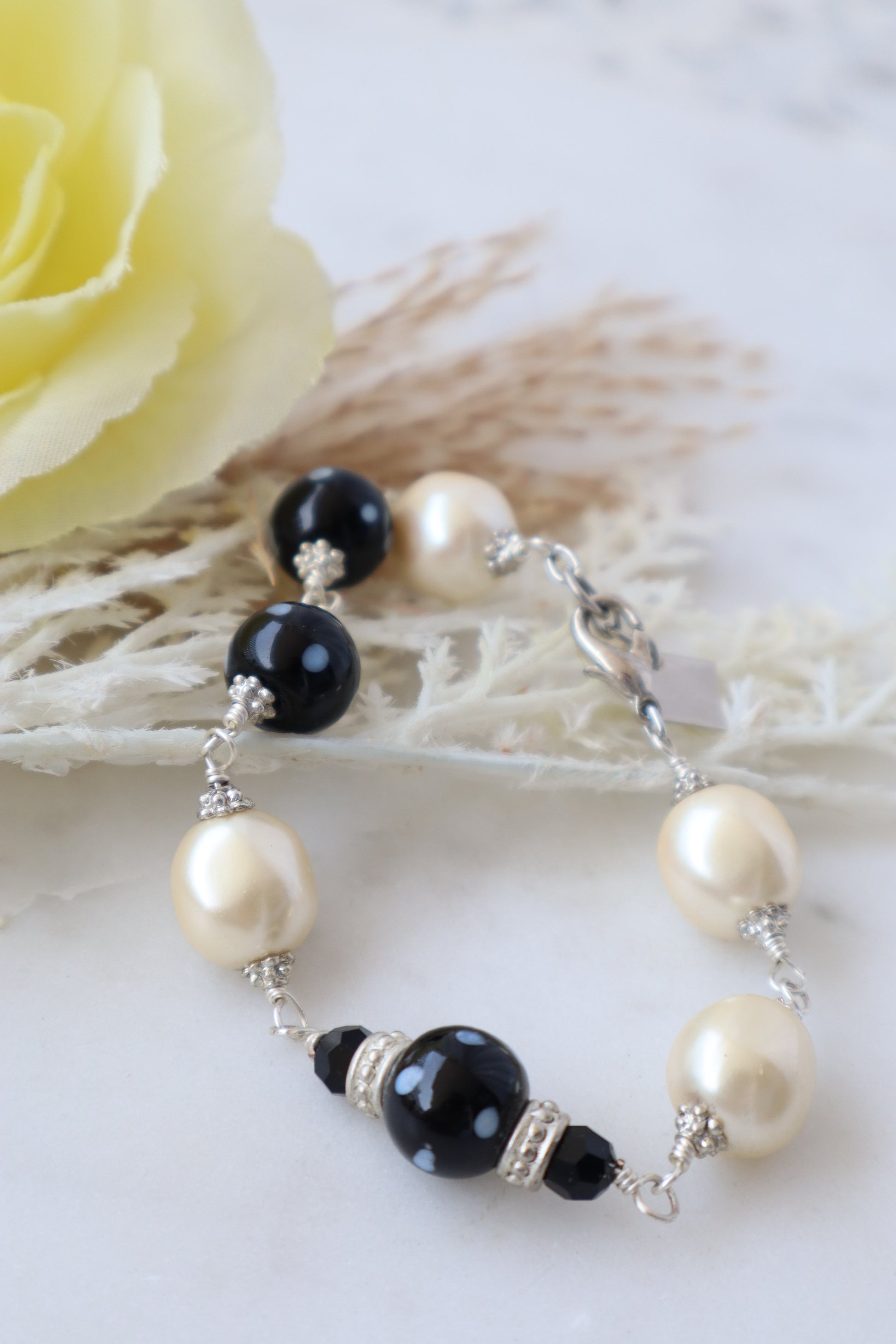 Pearl and black beaded bracelet on a white background with a yellow flower.