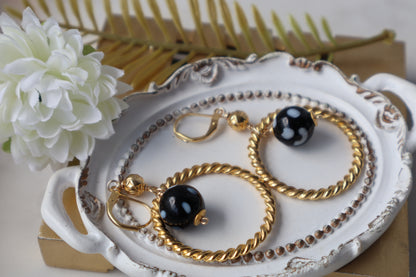 Gold and black jewelry set on a decorative plate with flowers and books in the background