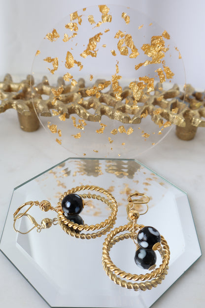 Gold hoop earrings with black stones on a hexagonal mirror with gold leaf accents.