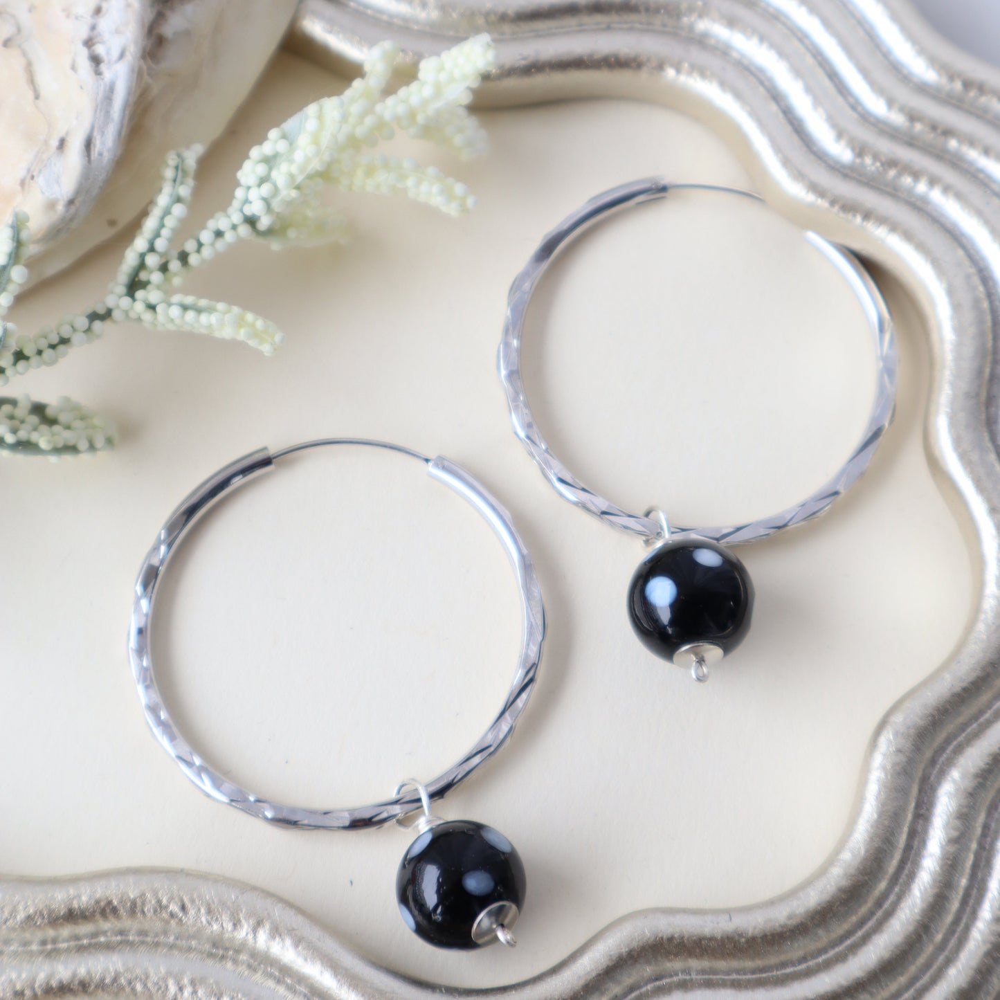 Silver hoop earrings with black beads on a textured white surface