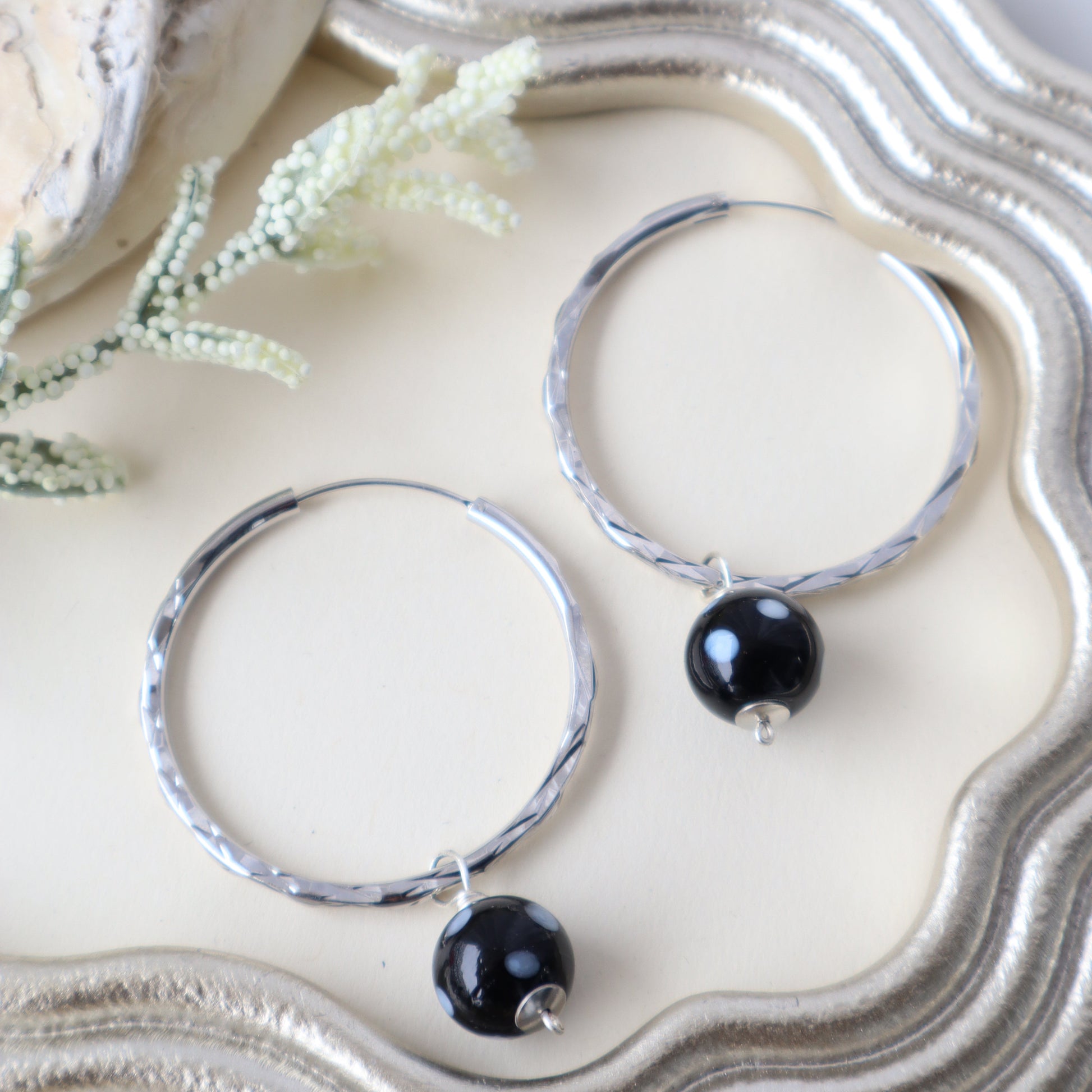Silver hoop earrings with black beads on a textured white surface