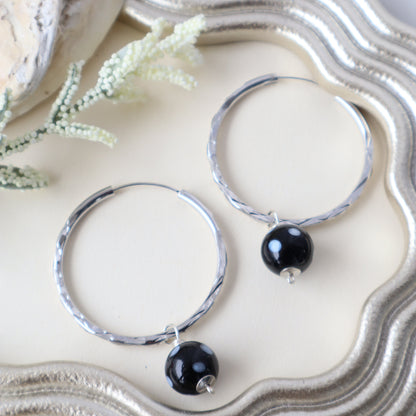 Silver hoop earrings with black beads on a textured white surface
