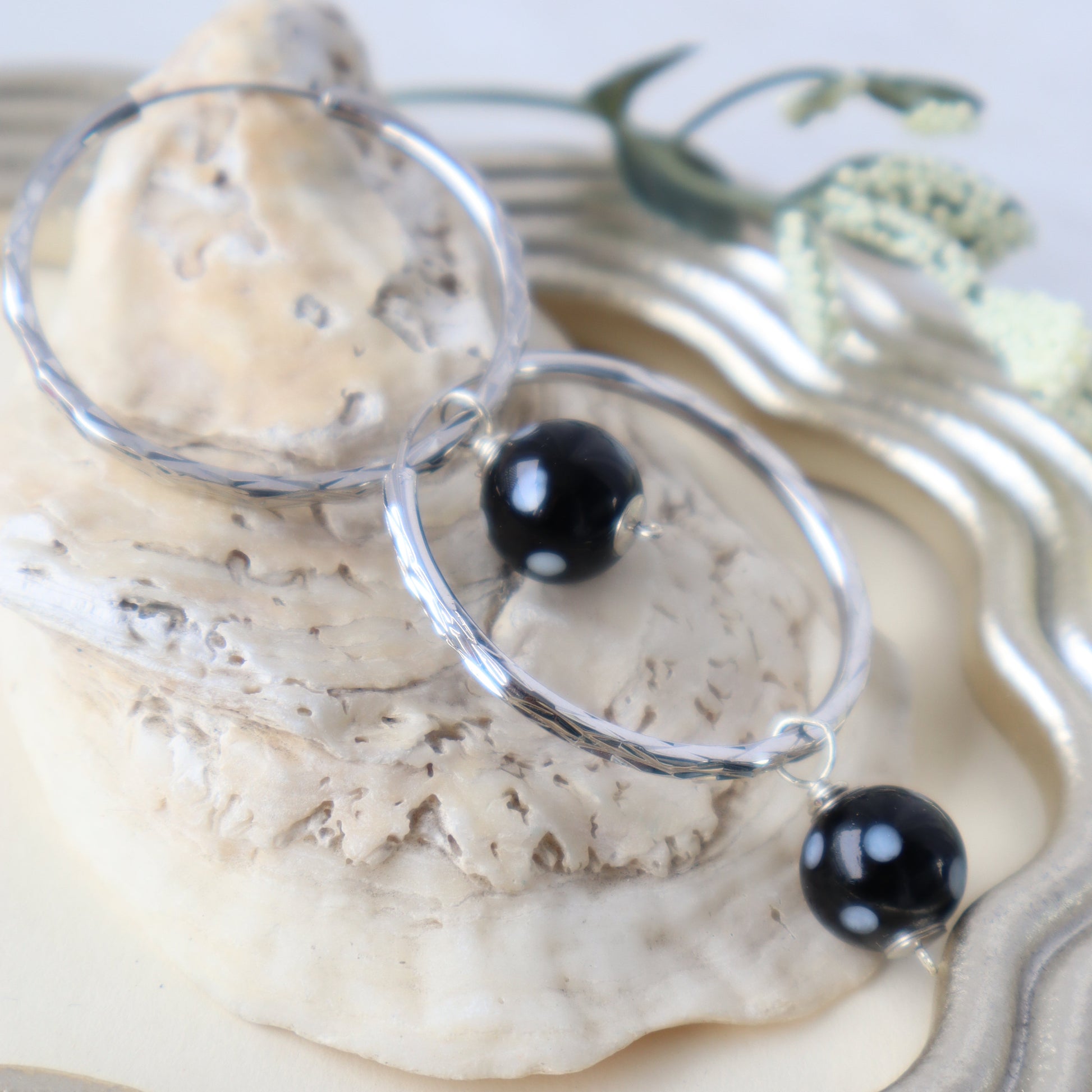 Silver earrings with black beads on a shell background