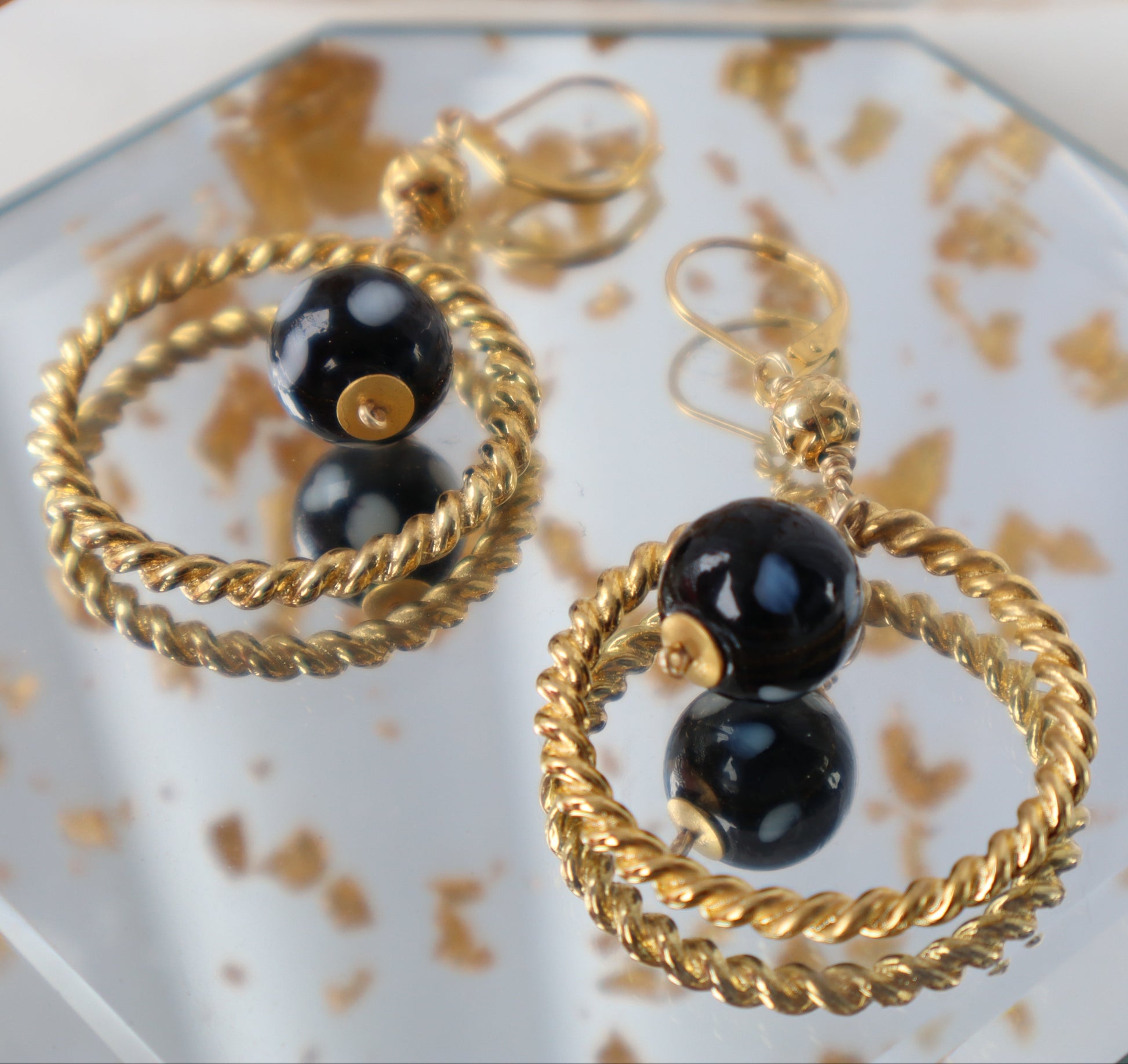 Gold hoop earrings with black beads on a decorative plate