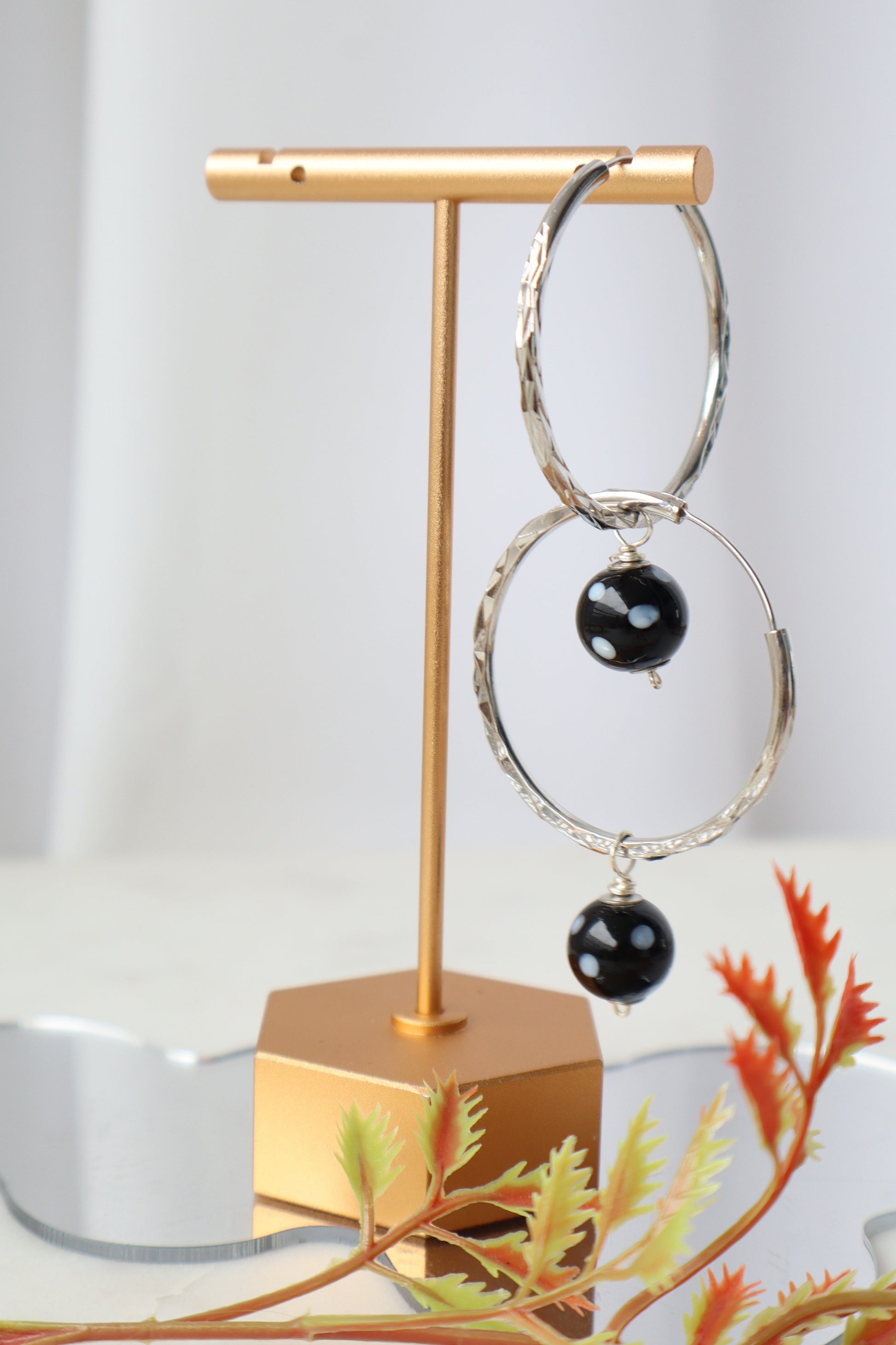 Gold and silver hoop earrings with black stones on a gold stand against a white background