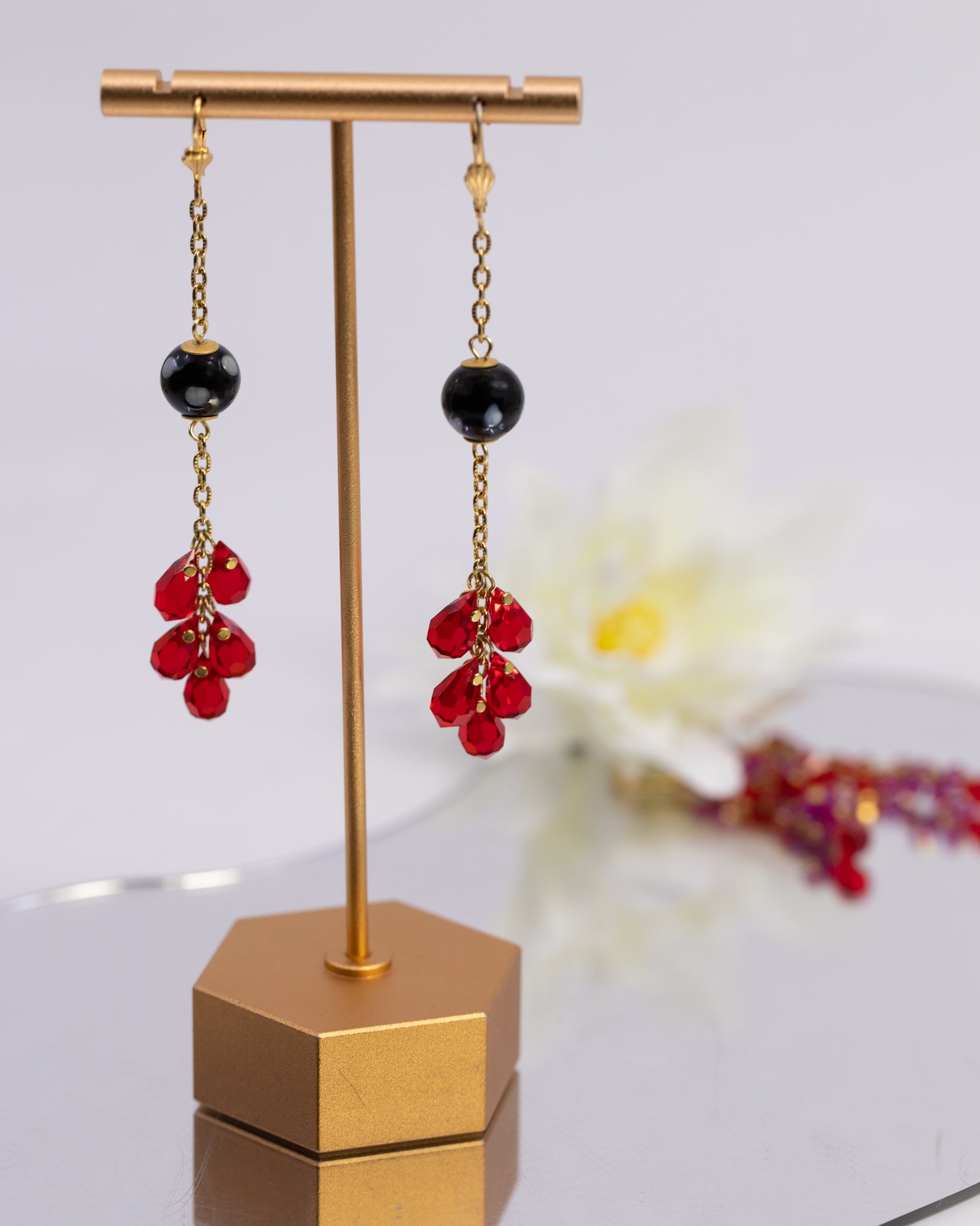 Pair of earrings with red beads and black stones on a gold stand.
