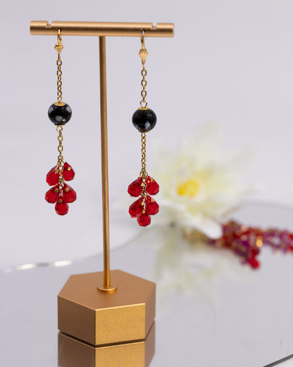 Pair of earrings with red beads and black stones on a gold stand.