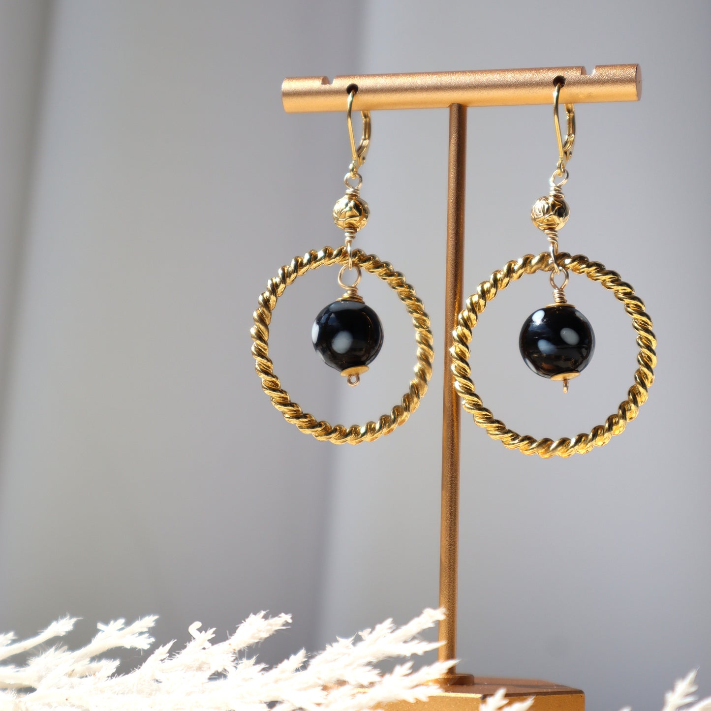 Gold hoop earrings with black beads on a gold stand against a gray background