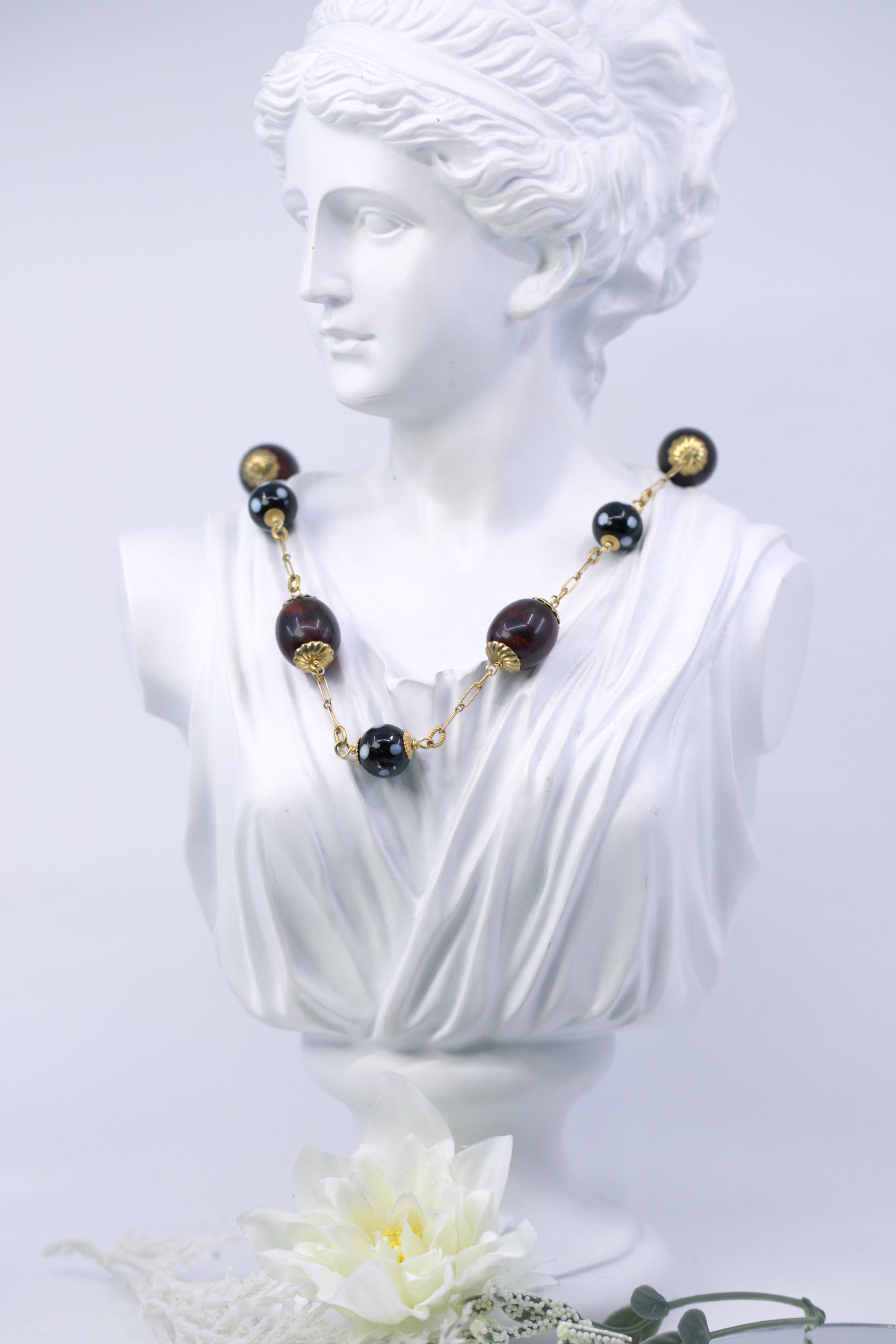 Necklace with black and gold beads on a classical bust against a white background