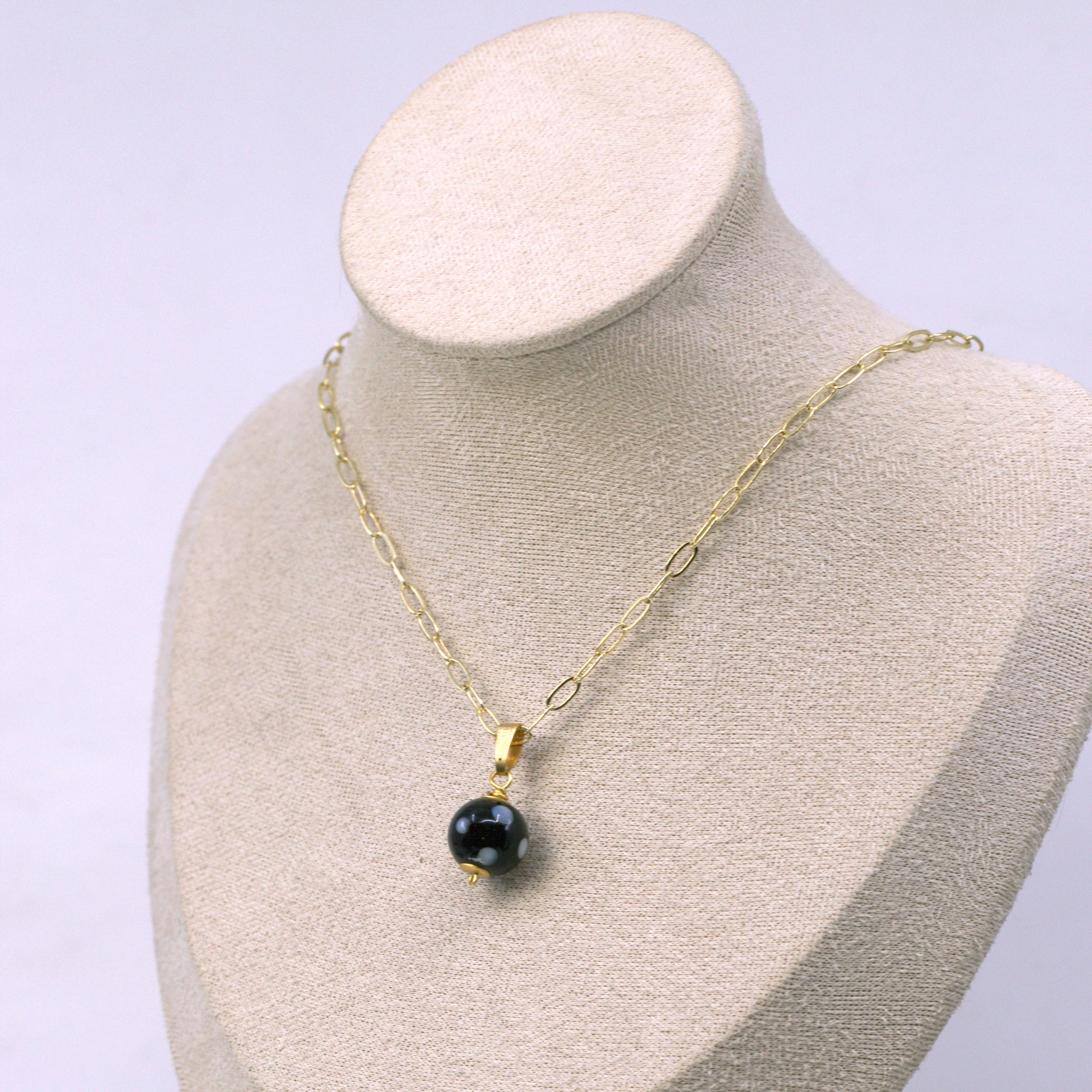 Gold necklace with a black pendant on a mannequin bust against a light purple background