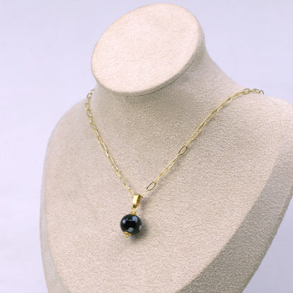Gold necklace with a black pendant on a mannequin bust against a light purple background