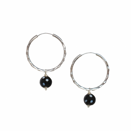 Silver hoop earrings with black evil eye charm, minimalist spiritual jewelry on white background.