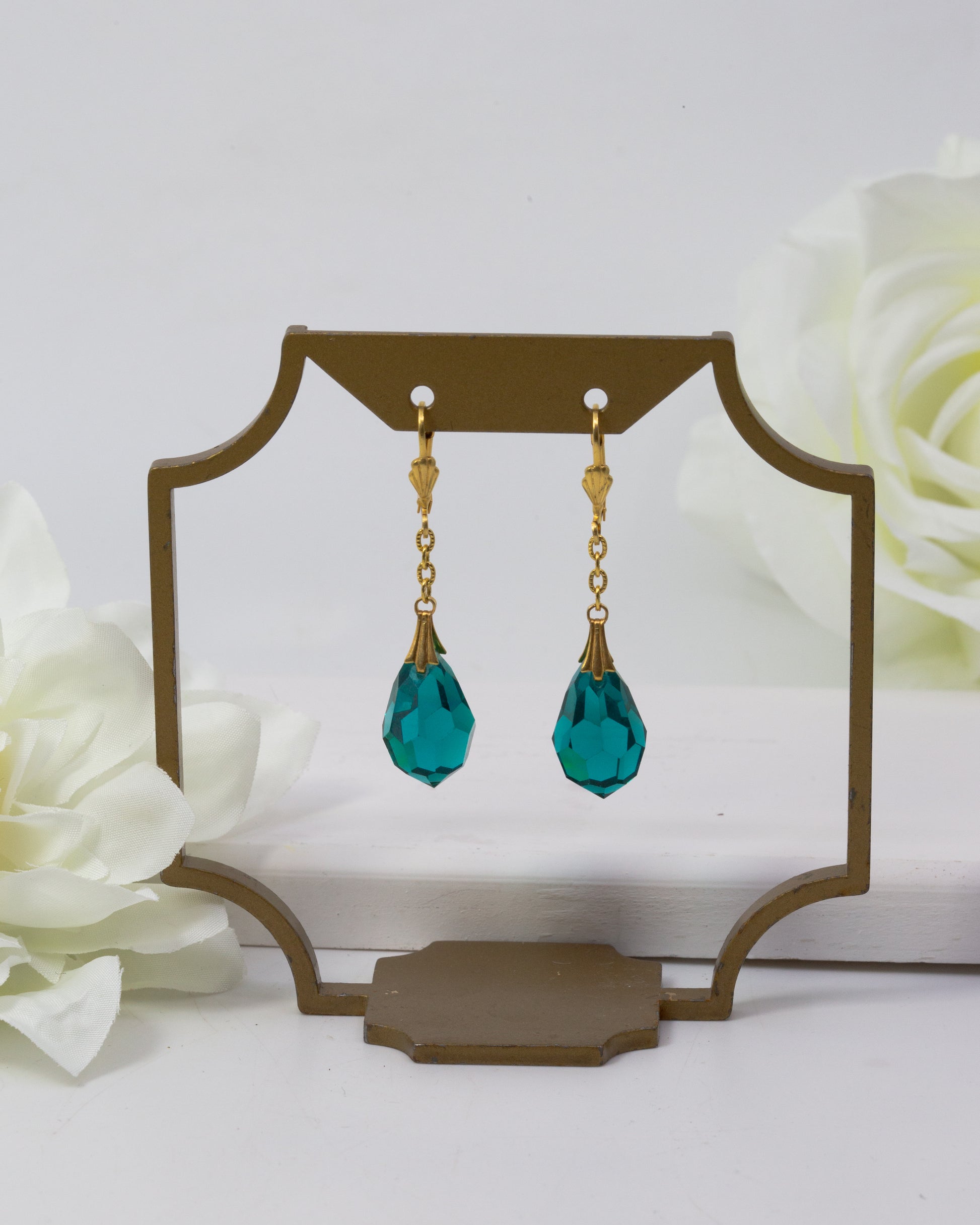 Teal drop earrings on a decorative stand with white flowers in the background