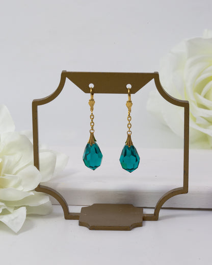 Teal drop earrings on a decorative stand with white flowers in the background