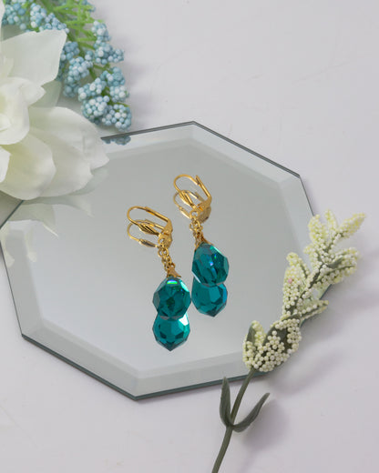 Gold earrings with teal beads on a decorative stand with flowers.