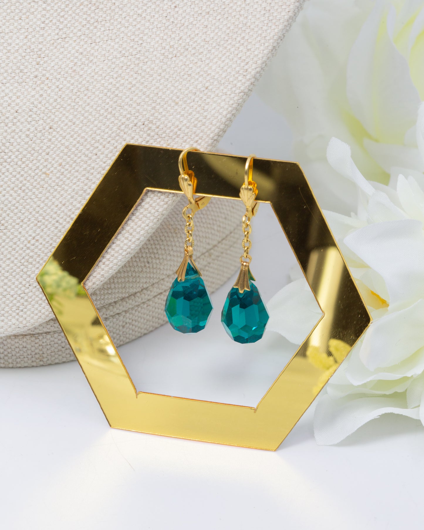 Gold earrings with teal drops on a hexagonal gold stand.