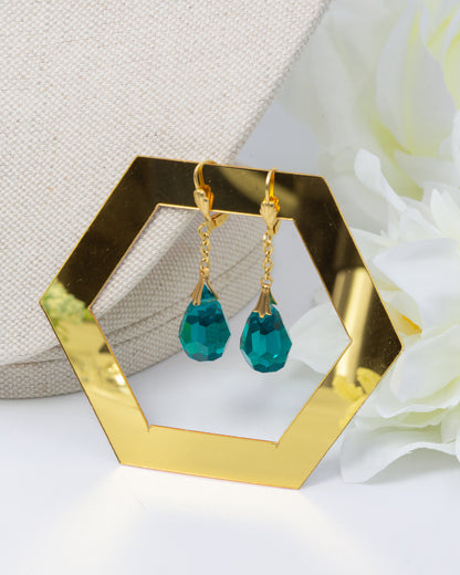 Gold earrings with teal drops on a hexagonal gold stand.