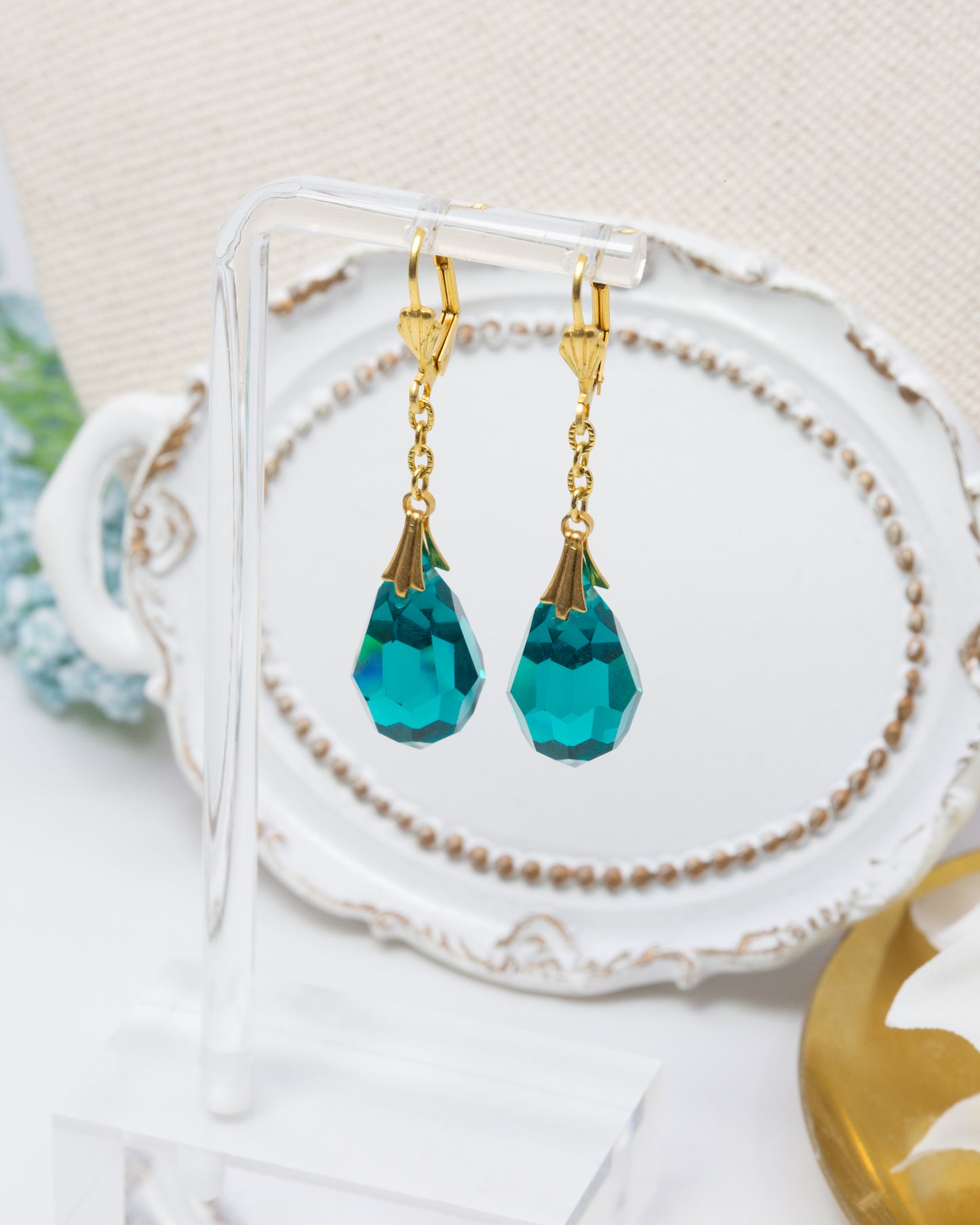 Teal drop earrings with gold hooks on a decorative stand.