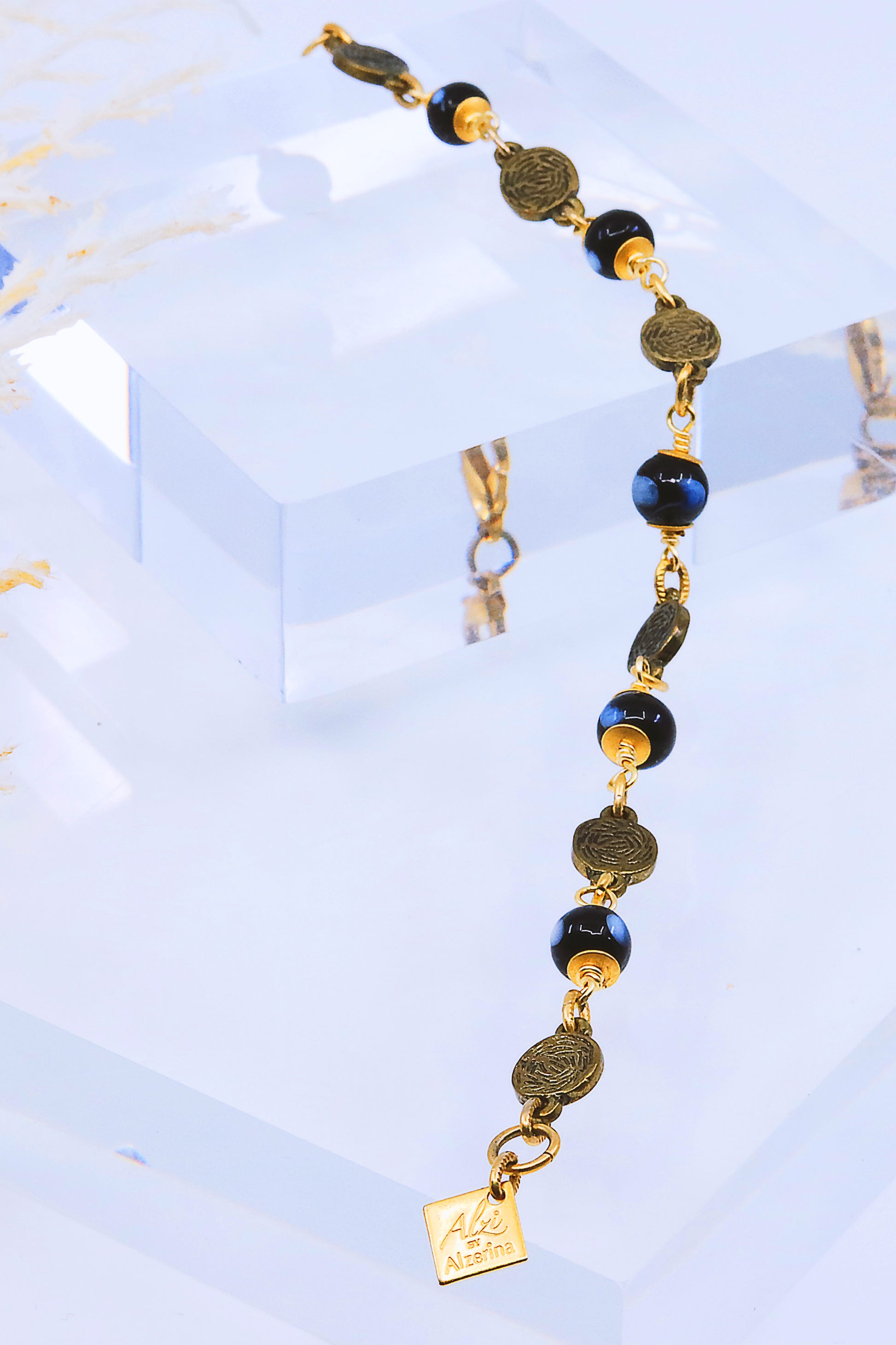 Gold and black beaded bracelet displayed on clear acrylic stand under bright lighting